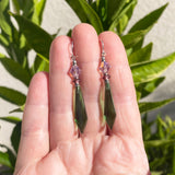 Green and purple earrings held in a hand with a plant background