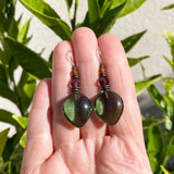Green glass earrings held in a hand with a natural background