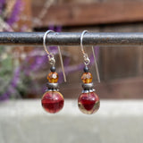 Pair of earrings with red and orange beads on a blurred background