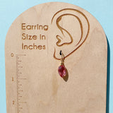 Wooden earring size gauge with a pink teardrop earring and measurement scale on a light blue background.