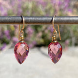 Pink teardrop earrings with gold hooks on a blurred natural background