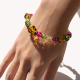A close-up of a hand wearing a colorful beaded bracelet with faceted amber, pink, green, and clear beads under bright sunlight.