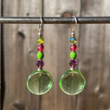 Pair of green round earrings with colorful beads hanging on a metal rod against a wooden background.