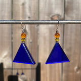 Blue triangle-shaped earrings with orange beads hanging on a rod against a wooden background.