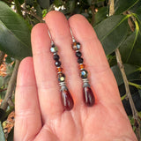 Beaded earrings held between fingers with a leafy background