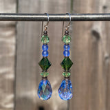 Pair of earrings with green and blue beads on a metal rod against a wooden background