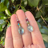 Hand holding a pair of beaded earrings with a green leafy background