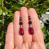 Red teardrop earrings on a hand with a green leafy background