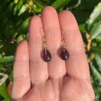 Amethyst earrings on a hand with a green leafy background