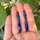 Blue beaded earrings held in a hand with a green leafy background