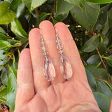 Clear teardrop earrings held in a hand with a green leafy background