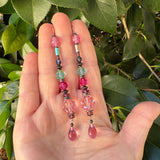 Hand holding a pair of colorful beaded earrings with a green leafy background