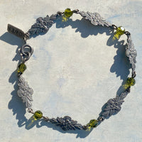 Silver bracelet with leaf designs and green beads on a light background