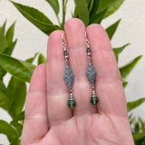 Silver earrings with green beads held in a hand against a leafy background