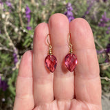 Pink teardrop earrings held between fingers with a blurred natural background