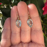 Gold earrings with aqua glass drops held between fingers against a natural background