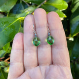 Green drop earrings held between fingers with a leafy background