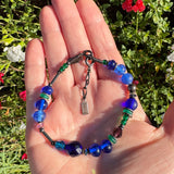 Blue glass bracelet held in a hand with flowers in the background. 