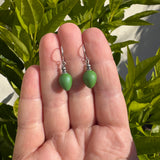 Green glass earrings held in a hand with a lime tree in the background.