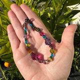 Hand holding a colorful beaded bracelet with a green leafy background