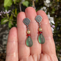 Silver earrings with green teardrop beads held between fingers against a natural background