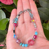 Beaded bracelet with pink and blue beads held in a hand against a green leafy background