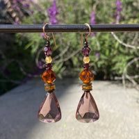 Light amethyst dangle earrings. Mauve German glass with Austrian crystal in topaz and amethyst. Czech glass in shades of light topaz. Metal trim is antiqued bronze, from our own tooling. All handwork done in the USA.