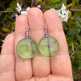 Green glass pink crystal earrings held in a hand.