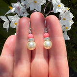 Pearl earrings held in hand with flowers in the background.
