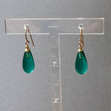 Green teardrop earrings on a clear stand against a gray background