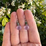 Frosted purple earrings in a hand with floral background. 