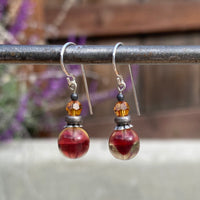 Pair of earrings with red and orange beads on a blurred background