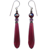 A pair of long teardrop-shaped drop earrings in deep burgundy glass, featuring faceted purple beads and silver French hook findings, shown against a plain white background.