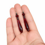 Garnet glass earrings held in a hand with a white background.