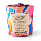 A pistachio milk candle in a container wrapped in a colorful abstract paint-splatter pattern, with a cream-colored label in the center.