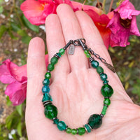 Green beaded bracelet on a hand with pink flowers in the background