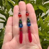 Frosted red glass earrings held in a hand. 