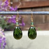 Green teardrop earrings with gold accents on a blurred natural background