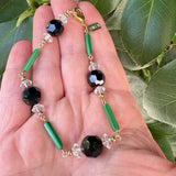Jet, crystal and green bracelet in a hand with a leafy background. Art Deco era glass.