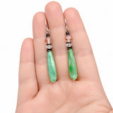 Jade glass earrings held in a hand with a white background. 