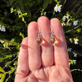 Clear yellow teardrop earrings on a hand with a natural background of greenery and white flowers.