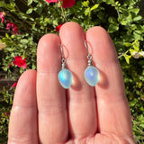 Opalite earrings held between fingers with a natural background