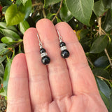 Black beaded earrings on a hand with a green leafy background