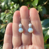 White beaded earrings on a hand with a green leafy background