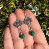 Green glass earrings held in a hand with a leafy background.