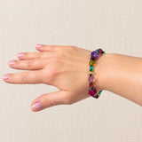 A multicolor beaded bracelet worn on a person's wrist, shown against a neutral beige textured background.