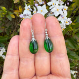 Emerald green dangle earrings. The earrings are held in a hand with a floral background. 