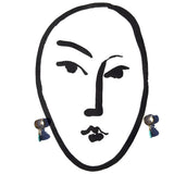 A pair of dangling earrings shown against a white background, with a minimalist black line drawing of a face used as a decorative graphic. The earrings have round metallic tops and drop down to light blue beads.