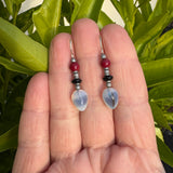 Pair of earrings held between fingers against a green leafy background