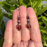 Pair of beaded earrings held between fingers with a green leafy background